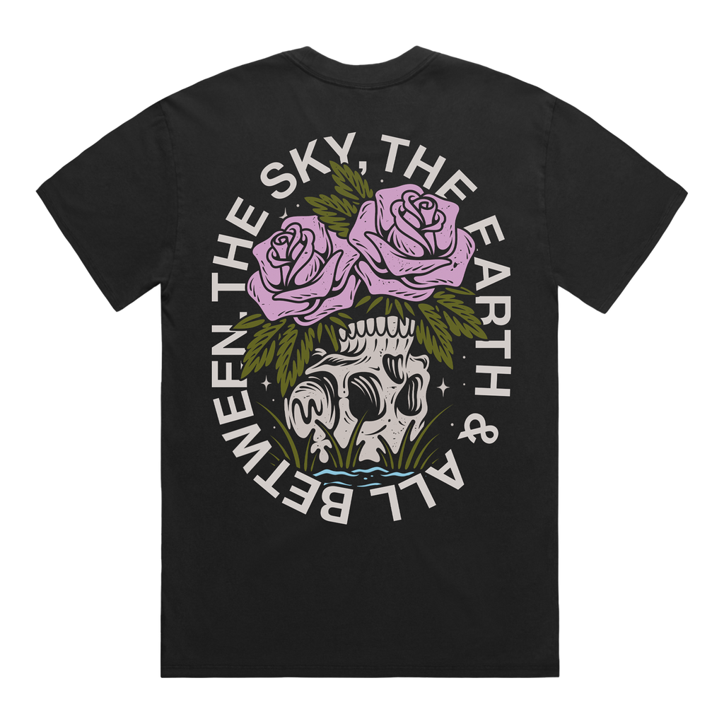 Back of a black short-sleeve t-shirt featuring a flower‚Äìskull graphic, with white text around it that reads ‚ÄúThe Sky, The Earth & All Between.‚Äù