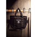 Black bag with 'ARCHITECTS' logo hanging on a wooden rack against a textured wall.